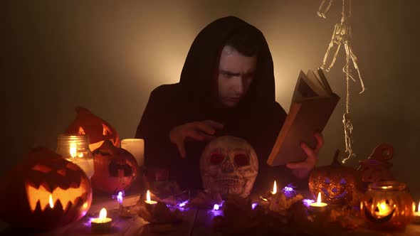 A Spooky Wizard is Reading a Magic Book and Conjuring Over the Skull on the Black Background