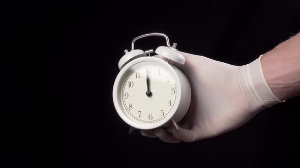 Close-up alarm clock in hand in a medical glove 