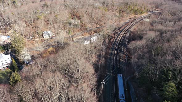 And aerial view over a silver train on a sunny day. There are brown, leafless trees all around and t