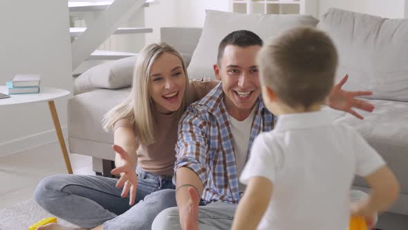 Happy Young Adult Parents with Child Playing on Floor in Modern Living Room