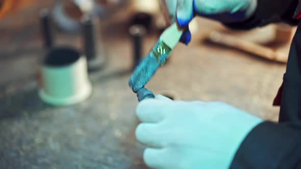 Close-up of man's hands with a brush painting metal tool with blue color in factory. 