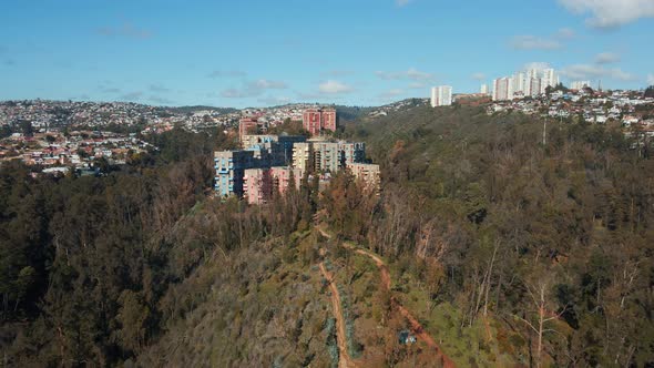Aerial dolly out of Quinta Vergara Park and colorful residencial buildings in hill covered in forest