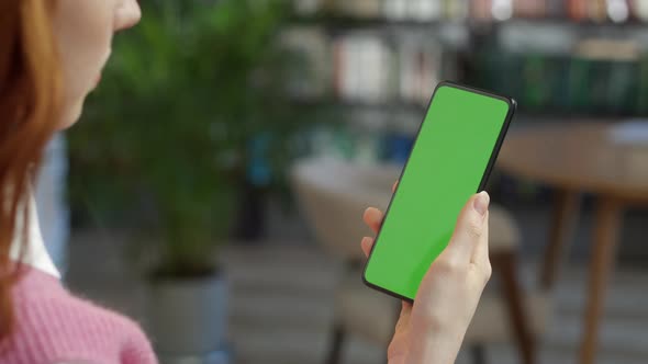 Back View of Redhead Woman Holding Chroma Key Green Screen Smartphone Watching Content With Touching alt