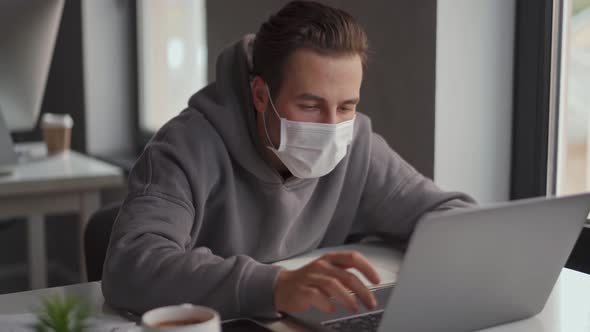 Confident man in protective mask working on laptop