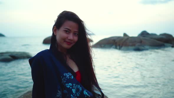 Cute Smiling Asian Girl Sitting on a Rock at Sunset in Slow Motion Thailand