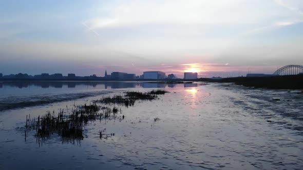 slow drone dolly shot of a reflection of the sunrise first in mud later in the water in the netherla