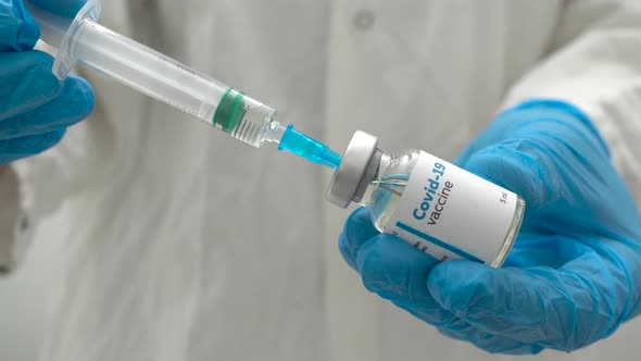 Close up of a doctor in medical blue gloves filling a syringe with a dose of coronavirus vaccine