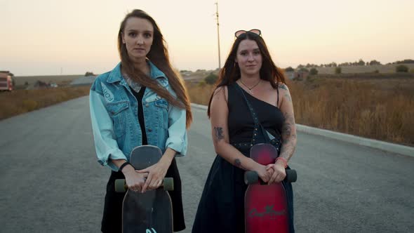 Two Young Ladies Are Standing on the Road and Holding Their Longboards, 