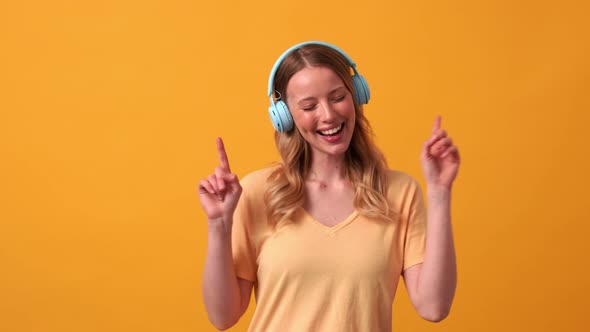 Happy blonde woman wearing yellow t-shirt listening music in headphones