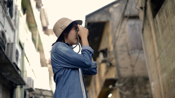 Attractive Asian woman traveler wearing retro fedora hat use film camera taking a photo.