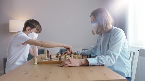 Father and Son in Medical Mask on Selfisolation They Play Chess Sitting in the Living Room