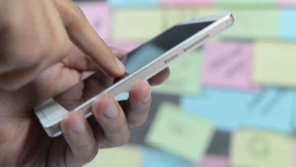 Man Using Phone, Sticky Notes Wall in Background