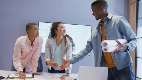 Three diverse male and female architects standing at table shaking hands in meeting room