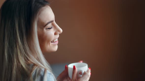 Happy Young Blonde Girl Relaxing Holding Cup of Hot Beverage at Light Studio Background Closeup