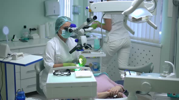 Focused Professional Orthodontist Curing Ill Tooth Examining Cavity with Dental Microscope As