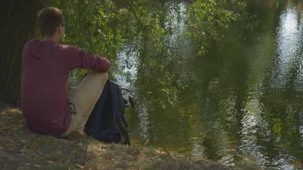 Man With Backpack Comes to River Bank Sits to The