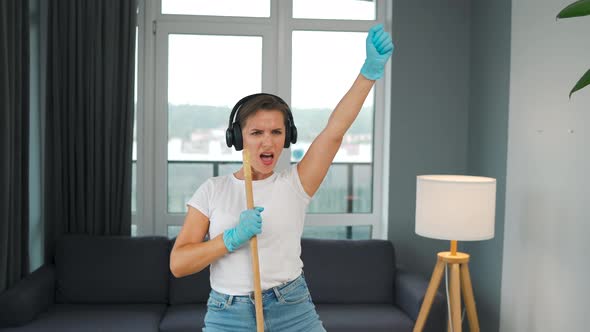 Woman in Headphones Cleans the House and Have Fun Singing with a Broom Like a Star at a Concert