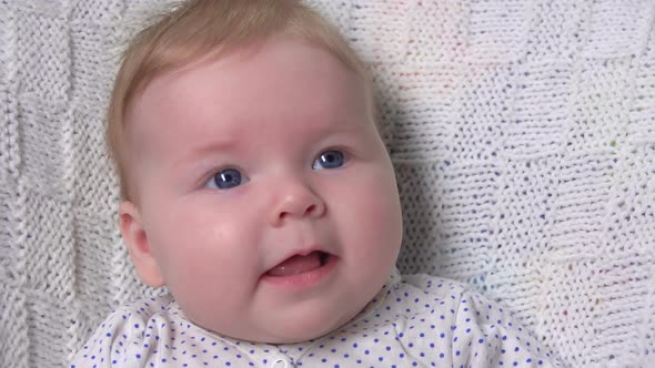 A Cute Little Blue-eyed Baby on a Knitted Blanket Is Laughing at the Camera