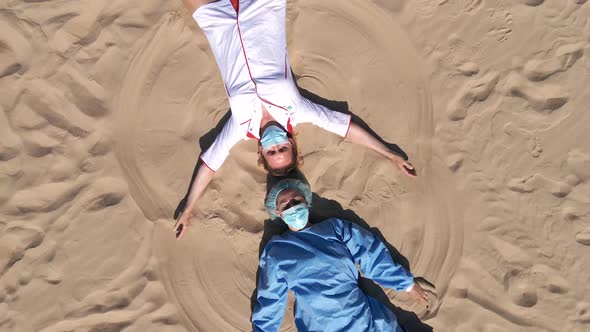 Funny: Two Female Doctors in Medical Gear Make Sand Angels Lying on Beach