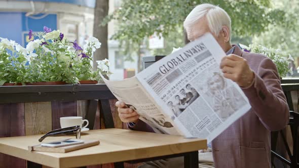 Senior Gentleman Reading Newspaper at Cafe Table