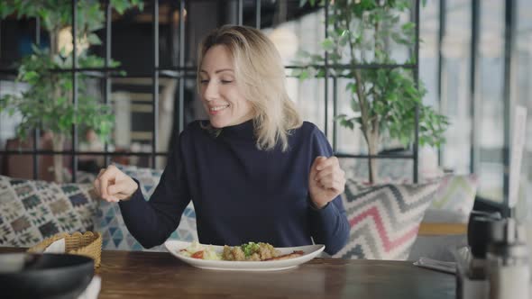 A Pleasant Blonde in a Restaurant is Happy to Eat a Dish of Fish and Rice