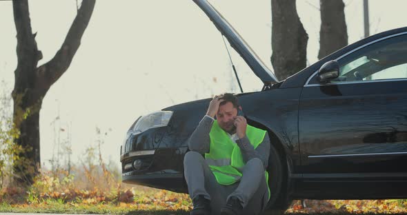 Sad Businessman Use Smartphone Sitting on Road Near the Broken Car Opened the Hood Calling Car