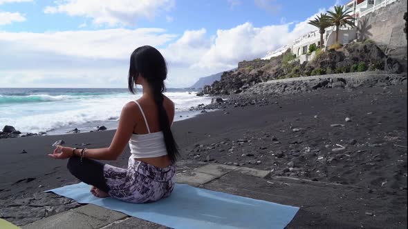 Woman in Sport Clothes Practicing Yoga and Meditating on Beach in Morning