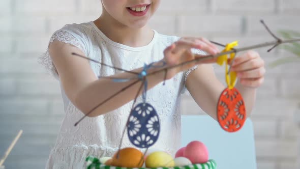 Smiling Girl Preparing Easter Decoration, Hanging Toy Eggs on Tree Branches, Eve
