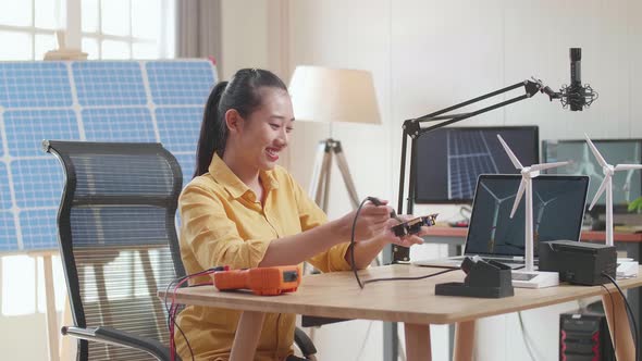 Asian Woman With Wind Turbine Fix The Circuit Board While Working With Laptop Next To The Solar Cell