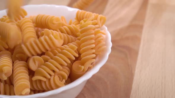 Organic vegetable lentil uncooked pasta fill a white bowl in slow motion