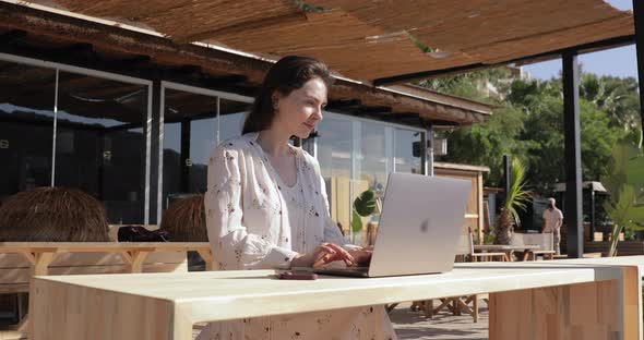 Freelance lifestyle. Girl relaxing on tropical beach terrace and doing remote work on laptop