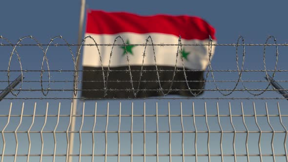 Blurred Waving Flag of Syria Behind Barbed Wire Fence