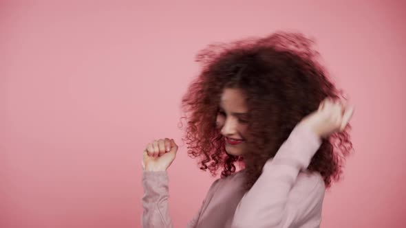 Beautiful Woman with Curly Hair Dancing with Head on Pink Studio Background. 