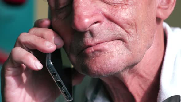 Close-up of an elderly Caucasian man listens attentively to his interlocutor while talking on a smar