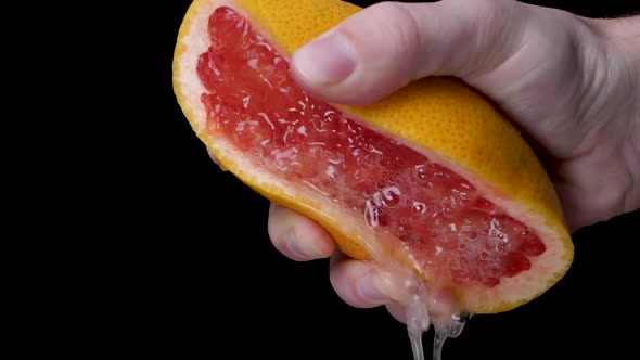 A white model is aggressively pressing out a juicy red orange grapefruit, a core spits out. In front