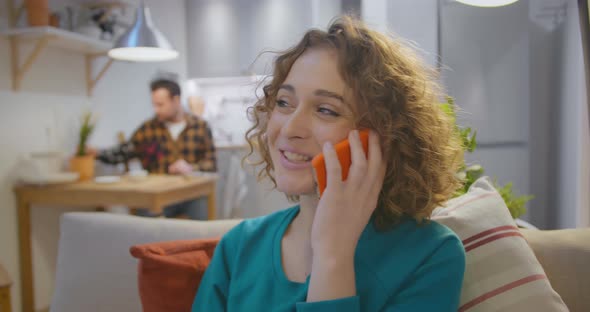 Happy Smiling Young Woman Sitting on Sofa and Calling on Smartphone Stay at Home