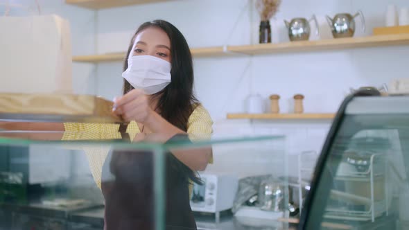 Attractive asian female cafe worker wears face mask and gloves giving takeaway food bag to custome