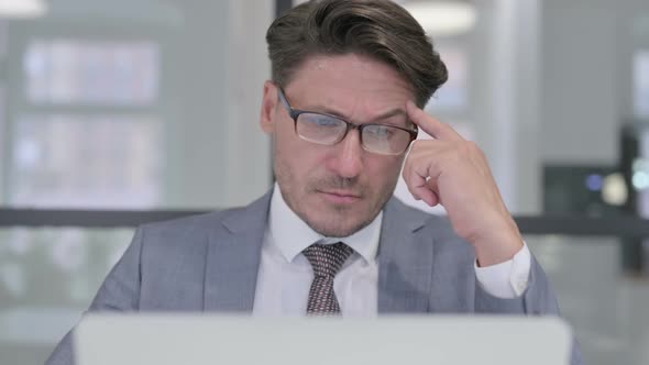 Portrait of Middle Aged Businessman Thinking and using Laptop