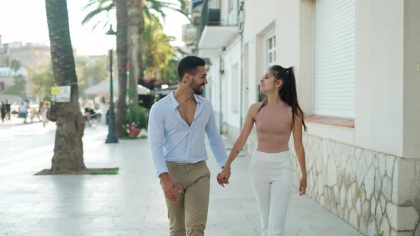 Smiling Hispanic Couple Holding Hands While Talking on Street
