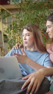 Two Young Beautiful Ladies are Searching Through the Internet on the Laptop Discussing and Smiling