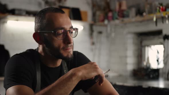 Male portrait: A man smokes a cigarette in a workshop.. The sculptor is tired and resting.