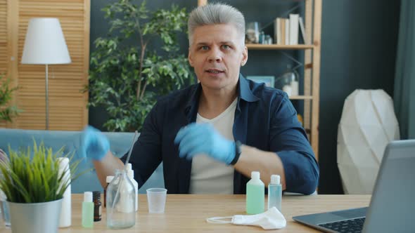 Portrait of Adult Man Making Hand Sanitizer at Home Holding Bottles Looking at Camera Talking alt