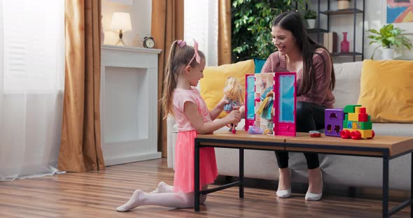 A Cheerful Mom is Playing with Pretty Daughter Dressed in a Pink Dress