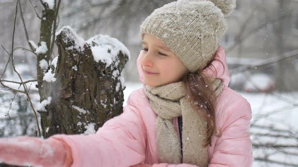 Winter Portrait of a Kid Girl in Pink Coat Wearing Beige Hat and Mittens Playing Outdoor in Snowy