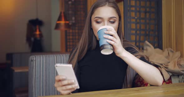 Young Pretty Woman in Casual Clothing Holding Cup of Coffee and Using Smartphone