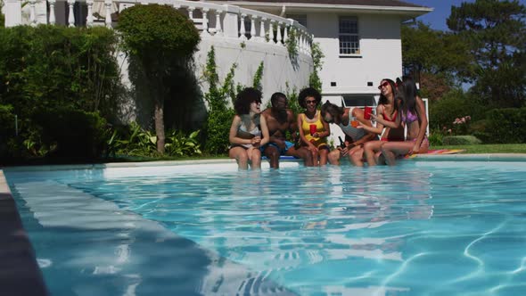 Group of diverse friends enjoying drinks while sitting by the pool