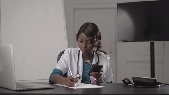 Attractive African Medical Doctor Talking on Telephone, in Cabinet Hospital, Write Diagnosis