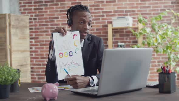 Black man businessman sitting at an office table holds a sheet with diagrams