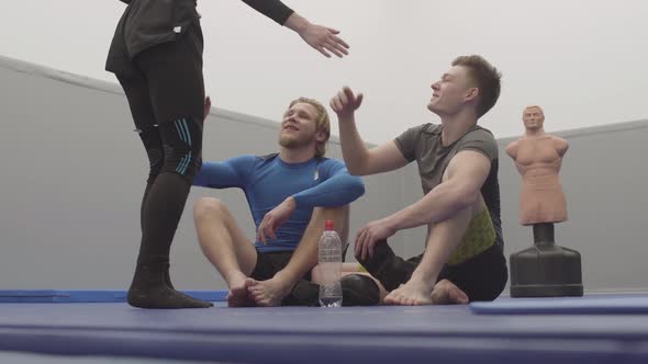 Two Athletic Men Sitting on the Floor in the Gym Resting After Training. The Dummy Is in the