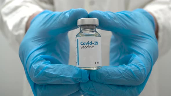 Doctor's hands in blue medical gloves holding a dose of coronavirus vaccine in a glass bottle